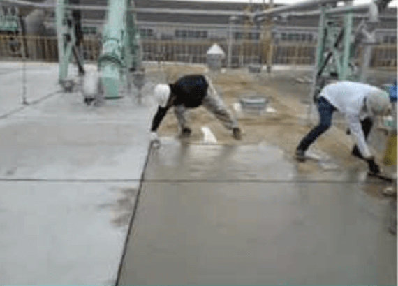 2 人の建設作業員が工業ビル内の新しい床のコンクリートを滑らかにしている。