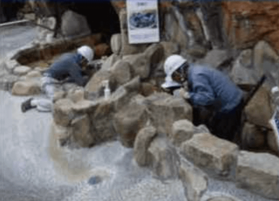 ヘルメットをかぶった2人の考古学者が発掘現場で古代の石造遺物を調べている。