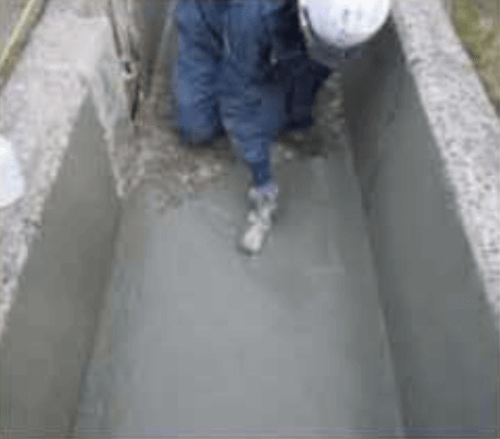 作業服とヘルメットを着用した作業員が狭いコンクリートの溝の中にしゃがみ込み、点検や修理を行っているようだった。